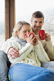 Couple in winter clothing drinking coffee against window