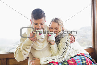 Loving couple in winter wear drinking coffee against window
