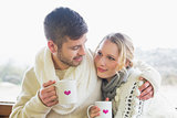Loving couple in winter wear with coffee cups against window