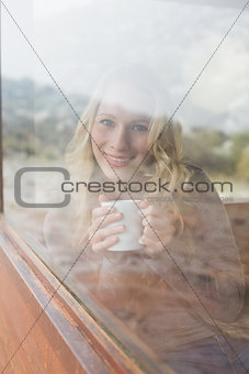 Content woman with coffee cup looking out through window