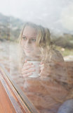 Thoughtful content woman with coffee cup looking out through window