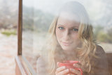 Content woman with coffee cup looking through window