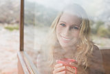 Happy woman with coffee cup looking through window