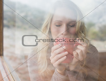 Woman drinking coffee with eyes closed through window