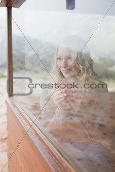 Thoughtful content woman with coffee cup looking through window