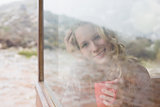 Happy woman with coffee cup looking through window