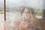 Thoughtful content couple with cups looking through window