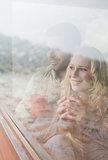 Thoughtful happy couple with coffee cups looking through window