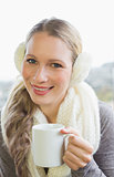 Smiling woman wearing earmuff with drinking coffee