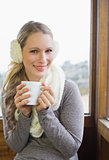 Smiling woman wearing earmuff with cup against window