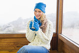 Cute woman with cup sitting in warm clothing against window