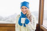 Woman with coffee cup in warm clothing against window
