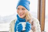 Woman with coffee cup in warm clothing against window