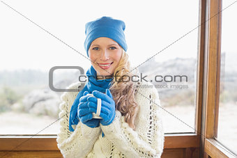 Woman with cup in warm clothing against window