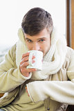 Man wearing earmuff while drinking coffee against window