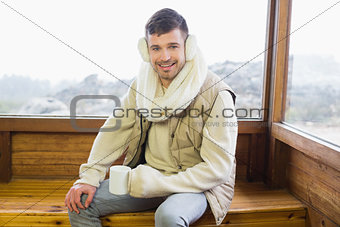 Smiling man wearing earmuff with coffee cup against window