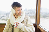 Thoughtful man wearing earmuff with cup against window