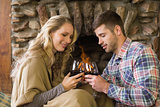 Couple toasting wineglasses in front of lit fireplace