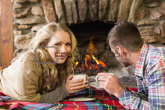Couple with tea cups in front of lit fireplace