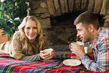 Smiling couple with tea cups in front of lit fireplace