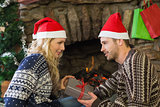 Man gifting woman in front of lit fireplace during Christmas