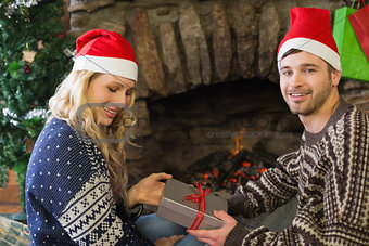 Man gifting woman in front of lit fireplace during Christmas