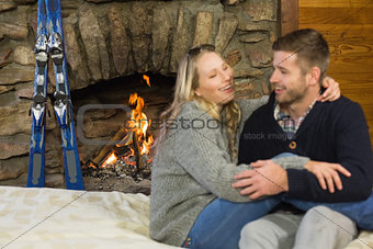 Cheerful couple with arms around in front of lit fireplace