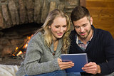 Couple using tablet PC in front of lit fireplace