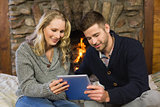 Couple using tablet PC in front of lit fireplace