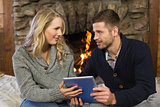 Couple using tablet PC in front of lit fireplace