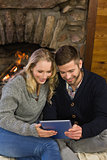 Lovely couple using tablet PC in front of lit fireplace