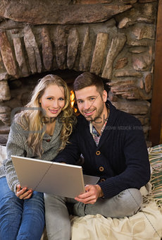 Lovely couple using laptop in front of lit fireplace