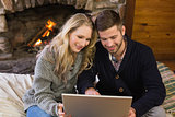 Couple using laptop in front of lit fireplace