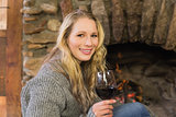 Beautiful woman with wineglass in front of lit fireplace