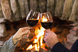 Hands toasting wineglasses in front of lit fireplace
