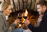 Couple toasting wineglasses in front of lit fireplace
