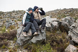 Couple sitting on rock with binoculars while on a hike