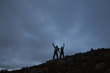 Couple raising hands on rocky landscape against sky at night