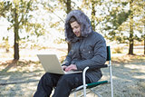 Man in warm clothing using laptop in the forest