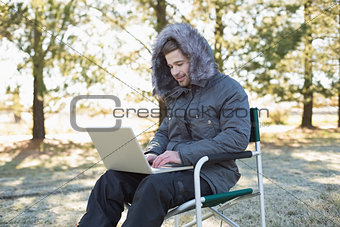 Man in warm clothing using laptop in the forest