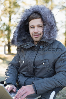 Young man in fur hood jacket using laptop in the forest