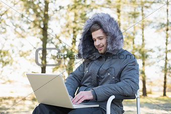 Young man in warm clothing using laptop in the forest