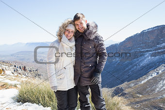 Smiling couple in fur hood jackets against mountain range