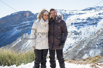 Smiling couple in fur hood jackets against snowed mountain range