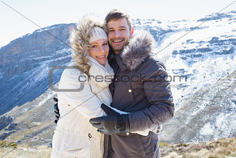 Loving couple in fur hood jackets against snowed mountain range