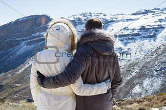 Couple in fur hood jackets looking at snowed mountain range