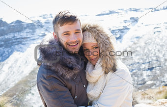Couple in jackets embracing against snowed mountain