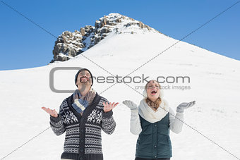 Cheerful couple with hands open looking up in front of snowed hill