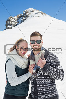 Smiling couple in warm clothing in front of snowed hill