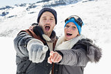 Couple in jackets pointing at the camera on snow covered landscape